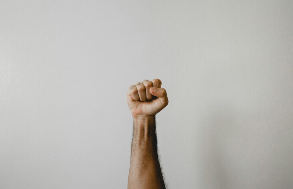 A person's arm raised with a clenched fist against a plain light background