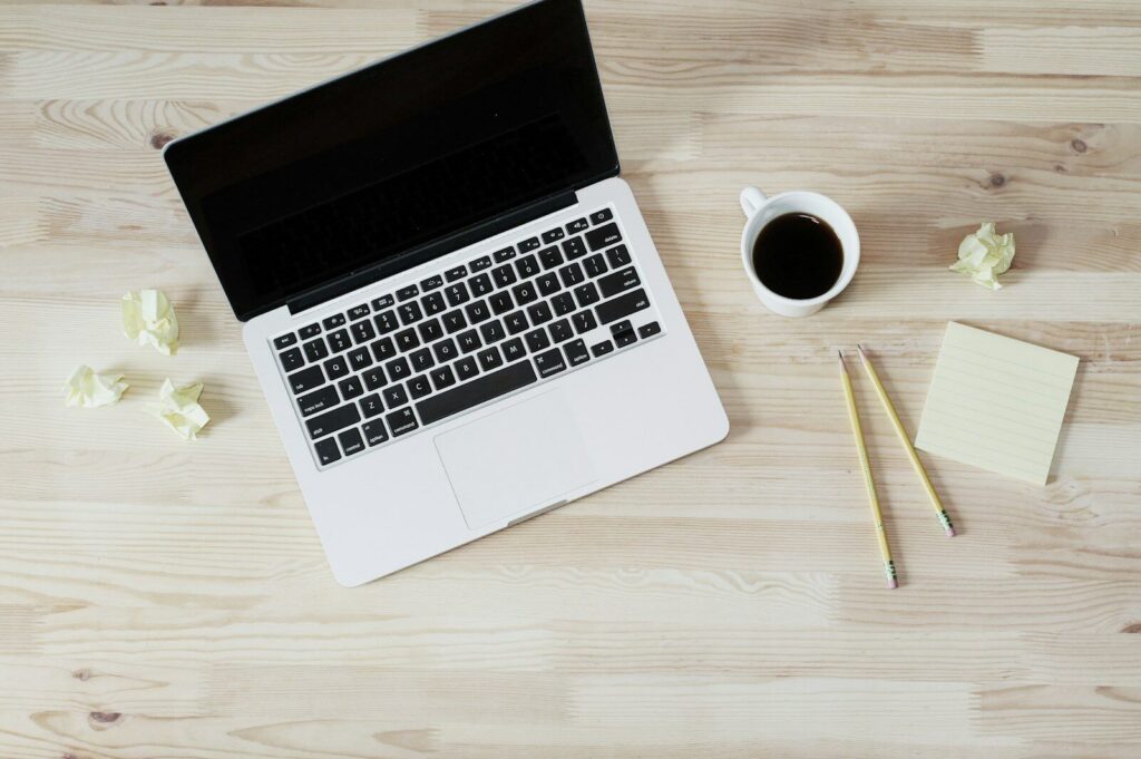 Laptop, coffee, sticky notes and crumpled paper on a desk, the hidden unpaid work of freelancing
